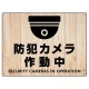 防犯カメラ作動中 (丸形イラスト)  白木調背景/黒文字 オリジナル プレート看板 W600×H450 エコユニボード W600×H450 エコユニボード