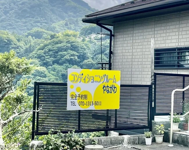 背景の自然に黄色の看板が一際目を引く整体院様のプレート看板を製作いたしました。