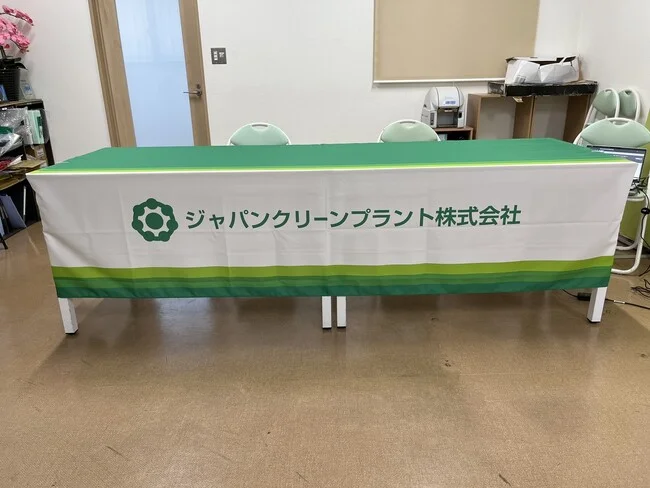 グリーン帯に社名が映えるクリーンエネルギー機器製造会社様のオリジナルテーブルクロスを製作いたしました。