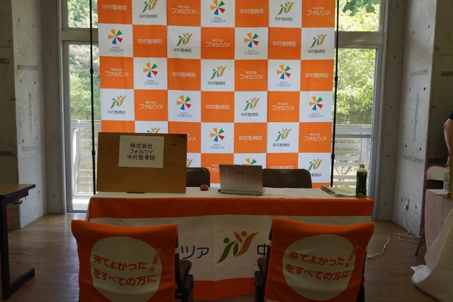 明るいオレンジ格子柄が目を引く介護福祉関連企業様のバックパネルを製作いたしました。